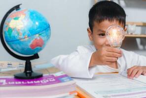 Boy holding a bright light bulb to represent new creativity, Education concept, Smart kid against green blackboard, Idea and creativity concept, Copy space for your text. photo