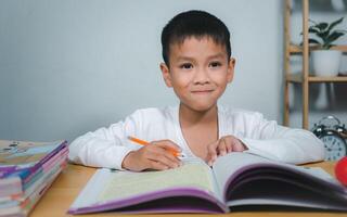 Education, Childhood, People, Homework and school concept. Student boy with book writing to notebook at home, Student learning study reading book while sitting at home. photo