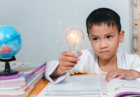 Education concept, Smart kid against green blackboard, Boy holding a bright light bulb to represent new creativity, Idea and creativity concept, Copy space for your text. photo