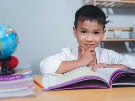 The child smile thinking sitting at table with book. Education, Childhood, People, Homework and school concept. Student learning study reading book while sitting at home. photo