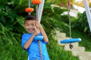 Asian boy happily playing on a swing climbing rope with playground equipment. Soft and selective focus. photo