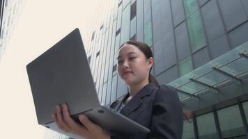 Asian Young businesswoman using laptop working behind high-rise building, concept of working with young people and technology. video
