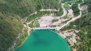 Aerial view of a hydro power plant with a turquoise reservoir, set amidst lush green forest and rugged terrain video