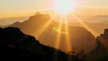 uma imagem perfeita cena do uma nascer do sol sobre a montanhas com lente chamas dançando através a céu e iluminador a áspero terreno abaixo. luz vazamentos bokeh. video