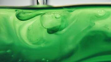 A vibrant green liquid remaining suspended in the center while a lighter liquid is separated and skimmed off the top.. video