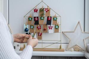Number on craft paper notes with tasks before Christmas holidays. Female making kraft paper for handmade advent calendar Made with your own hands step by step DIY crafts do it yourself photo
