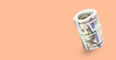 Roll Of One Hundred Dollar Bills Secured with a Rubber Band on a Peach Fuzz Background. photo