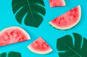 Tropical summer pattern made with fresh watermelon slices and green monstera leaves on bright blue background. Minimal summer fruit concept. Creative summertime exotic flat lay. photo