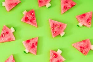Creative pattern composition with Christmas trees made of fresh watermelon slices on green background. Minimal Christmas or New Year concept. Trendy holiday fruit backdrop idea. Flat lay. photo