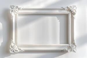 Antique carved white wooden rectangular picture frame on white wall background. Decorative elegant frame design with shadows. photo