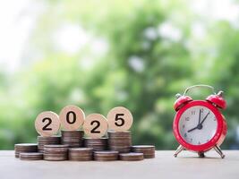 Red alarm clock, Wooden blocks with the number 2025 on stack of coins. The concept of saving money for manage time to success business in year 2025 photo
