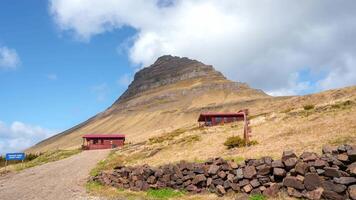 Iconic Kirkjufell mountain with its symmetrical shape and Kirkjufellsfoss waterfall cascading into a serene pool, bathed in warm sunlight under a partly cloudy sky. video