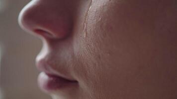 Close-up of a woman's cheek with a tear sliding down it. A tear slowly descends on the distressed face of a young girl, macro. video