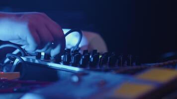 Close-up of the hands of a sound engineer adjusting the settings of a controller during the performance on a stage under the flashing concert light video