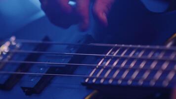 Nahansicht von das Hände von das Bass Spieler berühren das Saiten von ein Bass Gitarre während spielen ein heiter Lied auf das Felsen Show unter Konzert Beleuchtung video