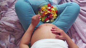 Top view of a pregnant woman eating a vegetable salad with a fork and stroking video