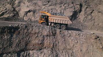 Large yellow dump truck loaded with rock is driving uphill along a quarry towards empty dump truck in a general view. Big heavy mining truck driving across the work site. video