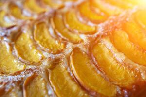 A close up of a dessert made of sliced peach. The dessert is covered in a caramel glaze and has a golden brown crust. The peach are arranged in a spiral pattern, creating a visually appealing photo