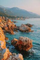 Rocky coastline at sunset with mountains near the ocean photo