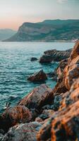 Rocky coastline at sunset with mountains in the background photo