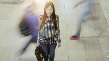 Young woman stands in modern hallway among crowd, exuding serenity in bustling urban setting video