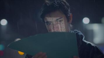 un hombre leyendo un documento en el lluvia a noche debajo un calle lámpara en un moderno paisaje urbano video