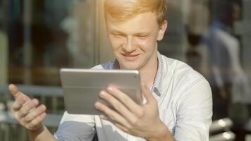 A young man is smiling and connecting through a tablet for a call in sunlight video