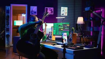 Professional composer teaching guitar lessons online on master class, recording himself playing acoustic instrument accords and explaining notes for tutorial. Young musician making vlogs. Camera B. video