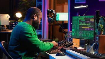 African american composer creating a new track for a project, using professional production pc interface in his home studio. Creative artist songwriter producing music with sound effects. Camera A. video