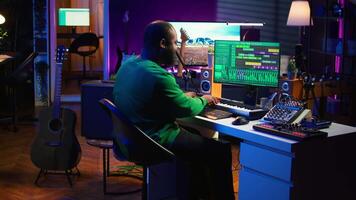 Audio engineer recording and producing new tunes on professional pc software, using mixing console and midi controller to create new music. Artist composer uses stereo gear at home studio. Camera B. video