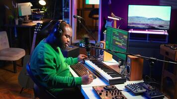 Talented famous composer writes down new verses and lyrics in home studio, composing music with digital software. Artist songwriter works with audio equipment and gear, recording tracks. Camera B. video