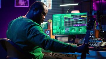 Producer composing new music on acoustic instrument in home studio, using microphone to sing chords. Musician songwriter works with mixing console and software, guitarist producing tunes. Camera A. video