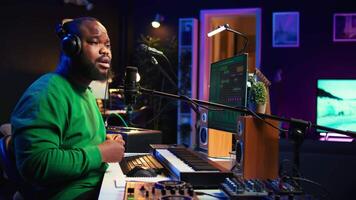 Confident artist singer performing a song on microphone in home studio, recording his audio files and manipulating raw sound on professional editing software. Music production. Camera B. video