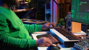 African american artist composing a new soundtrack for a project, using professional production software in home studio. Skilled creative singer producing music and adding sound effects. Camera A. video