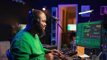 Young musician twisting knobs and mixing tunes with a console, following record settings on a digital software interface. Artist composer producing new music hits in his home studio. Camera B. video