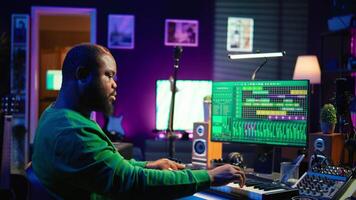 Skilled music producer creating new songs on midi controller synthesizer, working with mixing console and professional software on pc. Artist using piano and mastering acoustical tunes. Camera B. video