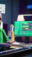 Vertical Musician doing online paid classes to help people play piano notes, teaching lessons from his home studio and recording tutorials. Musical instructor playing midi controller keyboard. Camera B. video