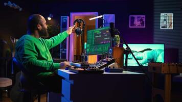Sound producer working with console and electronic keyboard to create perfect tracks for his songs, recording and editing audio. Music composer adjusts volume levels on pre amp knobs. Camera B. video