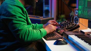 Skilled male composer producing new songs on his mixing console, operating on professional gear in home studio. Artist audio engineer twisting knobs to adjust sound levels on tracks. Camera A. video