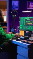Vertical Producer composing new track with electronic gear in his home studio, creating music on mixing console and software interface. Talented artist songwriter controls panel to produce sounds. Camera B. video