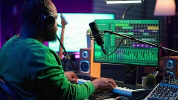 Young artist playing piano keys and singing song on microphone, composing his new music and mixing the tracks on digital interface. Producer technician composing melody with gear. Camera A. video