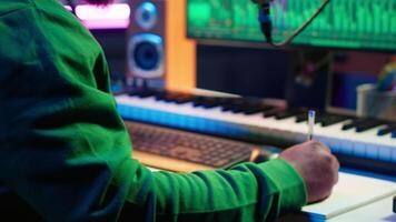 Talented famous composer writes down new verses and lyrics in home studio, composing music with digital software. Artist songwriter works with audio equipment and gear, recording tracks. Camera A. video