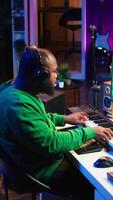 Vertical Musician playing piano keys and editing to improve sound quality of audio recordings in his home studio, putting on headset. Music producer uses midi controller to manipulate sounds. Camera B. video