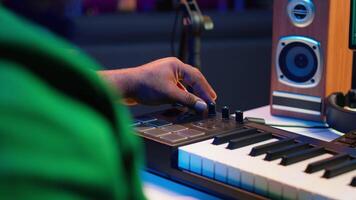 Music engineer producing song by mixing and mastering tunes on audio console, playing piano notes on synthesizer to record sounds on pc. Producer creating soundtracks with midi controller. Camera A. video