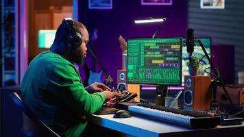 Confident music composer mixing sounds on digital audio software, creating a cool atmosphere in his home studio. Young cheerful producer composing new soundtracks with stereo gear. Camera A. video