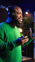 Vertical Singer performing his new track creation on a microphone, manipulates his audio files recordings with mixing and mastering techniques. Artist composer operates on stereo equipment. Camera B. video