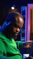 Vertical Producer composing new music on acoustic instrument in home studio, using microphone to sing chords. Musician songwriter works with mixing console and software, guitarist producing tunes. Camera B. video