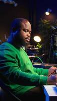 Vertical Composer writes verses and ideas to develop original song in home studio before recording new audio files. Songwriter using musical equipment and his imagination, artist composes music. Camera B. video