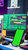 Vertical Young musician mixing and mastering songs next to isolated mockup display, operating on digital audio software to add sound effects on new tracks recorded. Audio engineer in home studio. Camera B. video