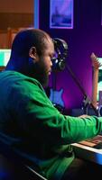 Vertical Songwriter mixing and mastering tracks on stereo console, playing electronic keyboard in home studio. Artist oversees audio performances to create melody, producing tunes with piano keys. Camera B. video